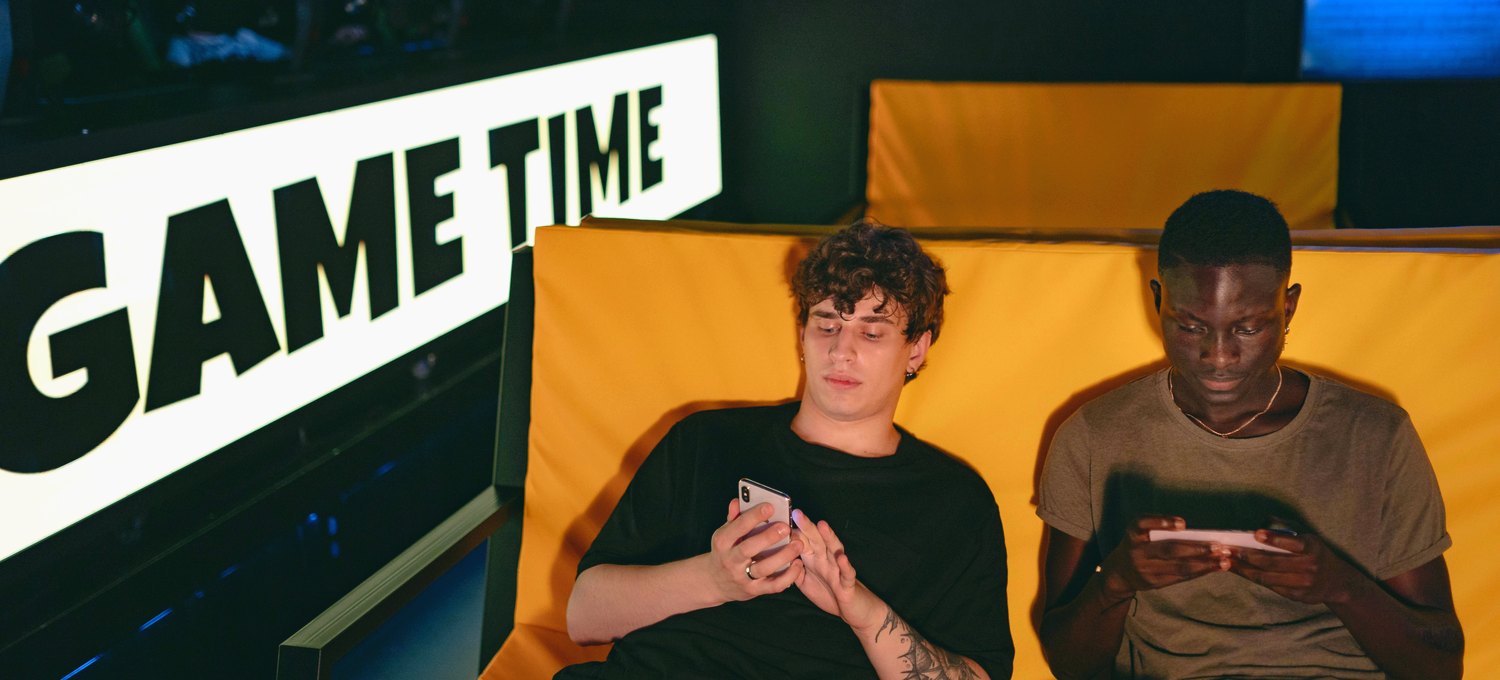 Two friends relaxing indoors and playing a game on their smartphones together.